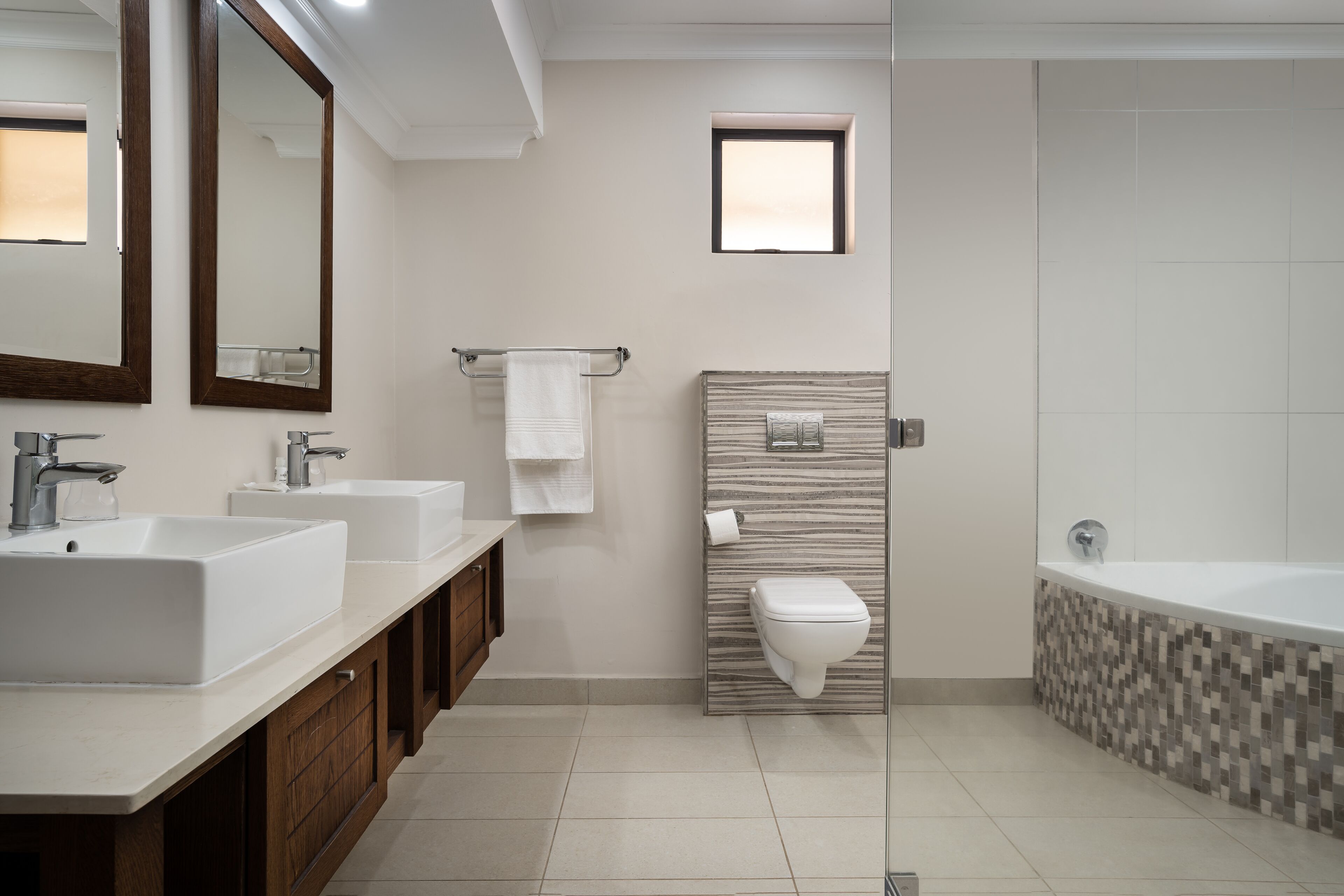 A modern bathroom with two sinks, a toilet, and a bathtub.