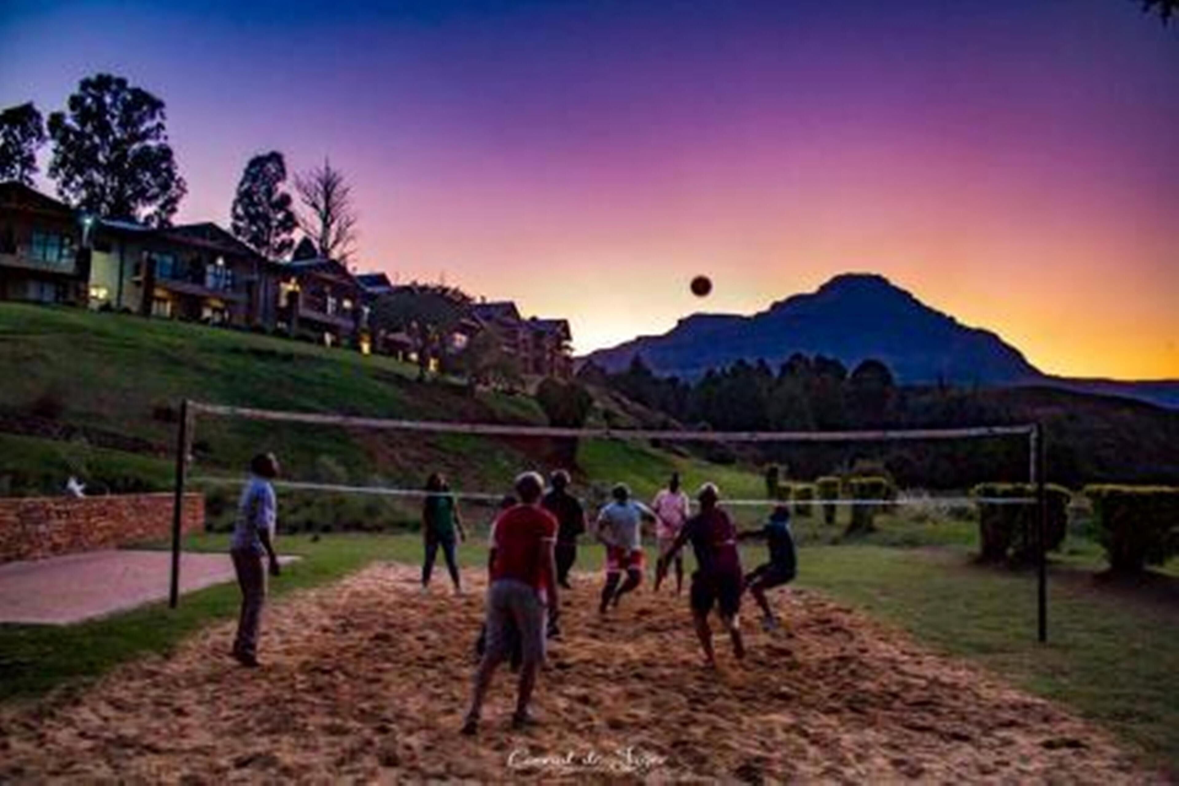 A group of people playing volleyball on a sandy court with a mountain in the background.