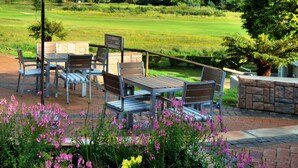 A patio with outdoor furniture, a table, and chairs, surrounded by flowers and a view of a green landscape with hills. - Premier Resort Sani Pass (Himeville)