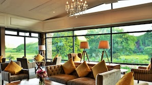 A spacious room with a large window offering a view of a lush green landscape. There are several sofas and chairs arranged around a wooden coffee table. - Premier Resort Sani Pass (Himeville)