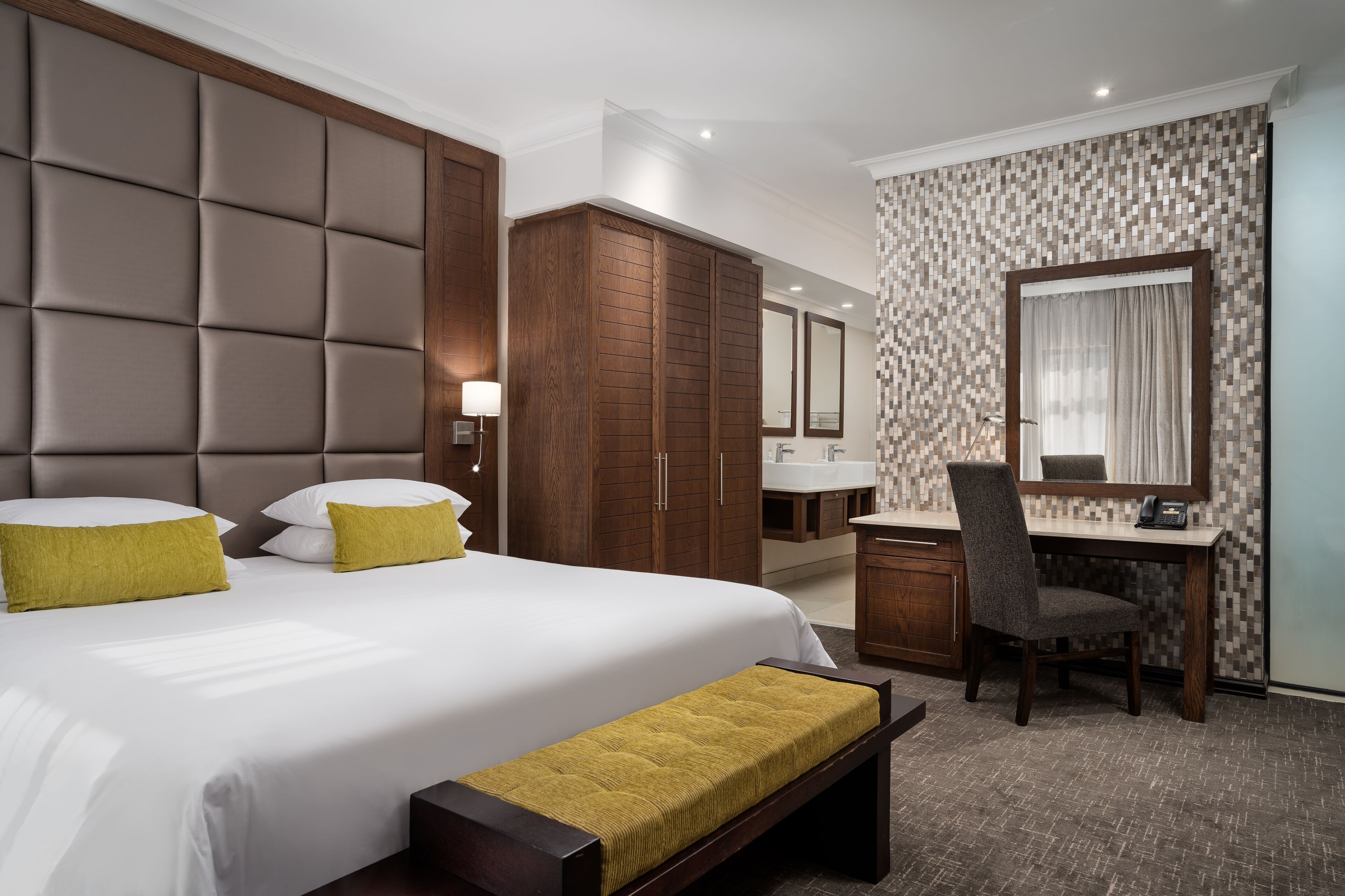 Habitación de hotel con una cama grande, un escritorio, una silla, un armario y un baño con pared de azulejos.