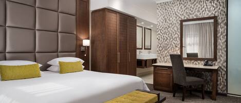 Habitación de hotel con una cama grande, un escritorio, una silla, un armario y un baño con pared de azulejos.