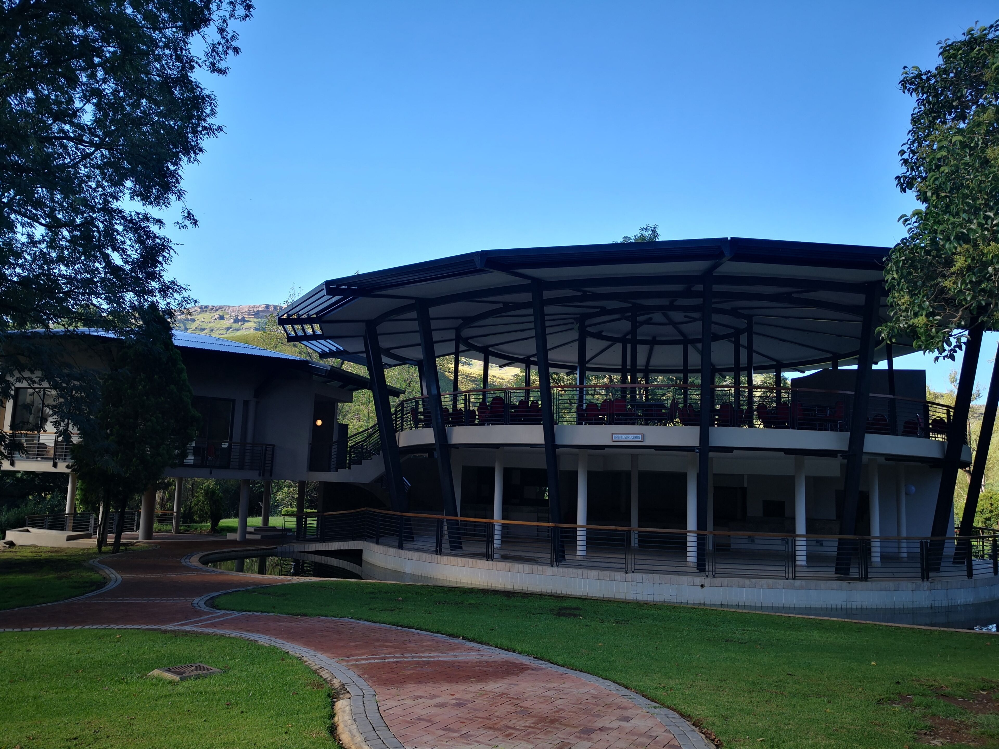 A modern building with a covered outdoor area, a curved pathway, and a view of a mountainous landscape.