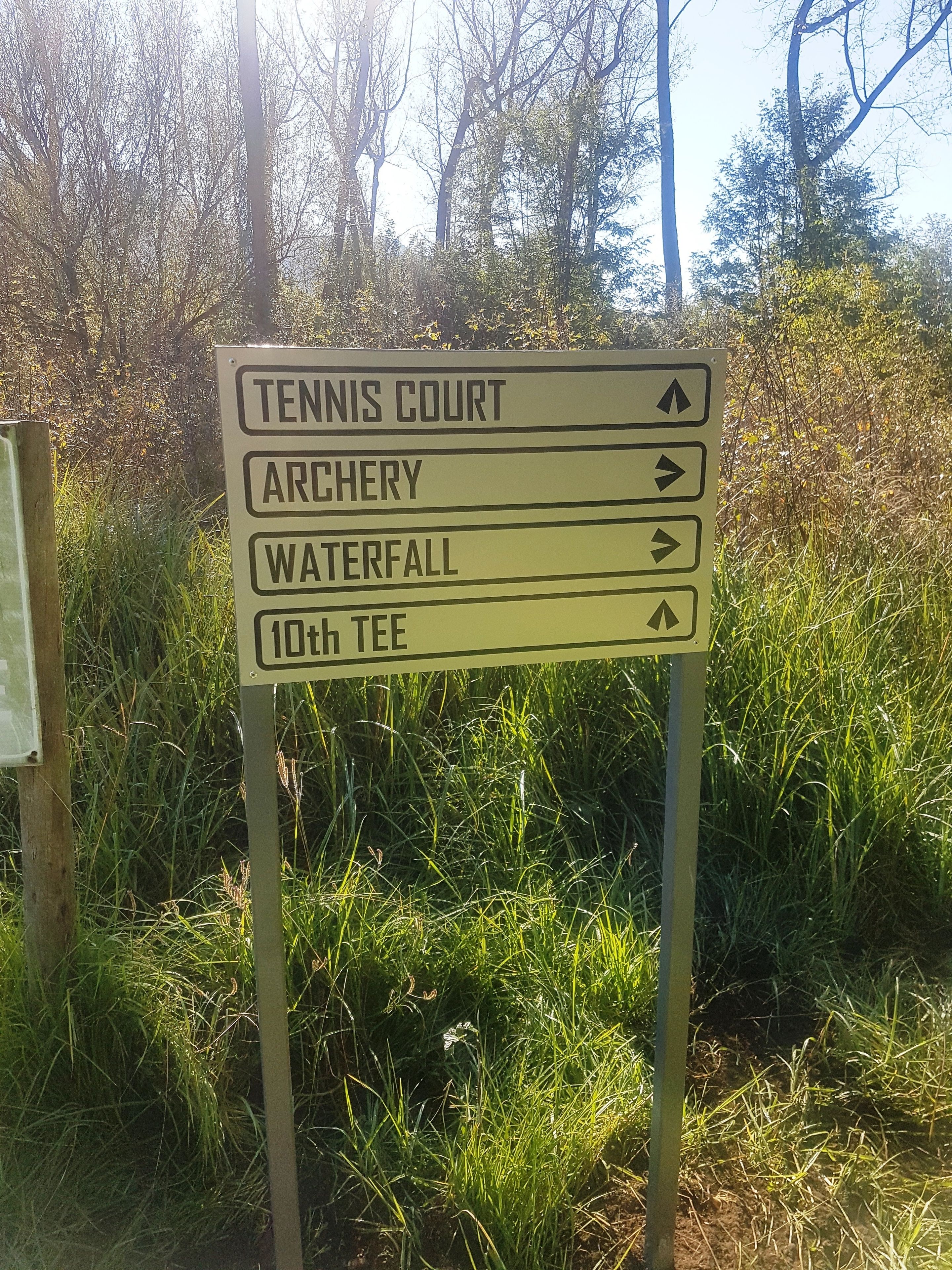 A directional sign with arrows pointing to Tennis Court, Archery, Waterfall, and 10th Tee.