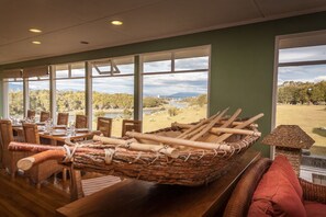 A dining area with a view of a lake and mountains, featuring wicker furniture and a woven basket with wooden paddles.