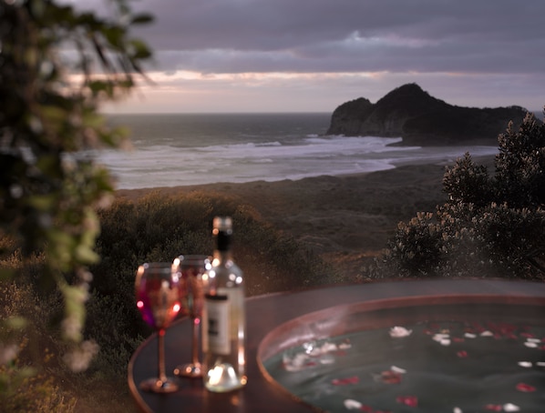 Una mesa con una botella y vasos, con vista a una playa y olas, y acantilados a lo lejos.