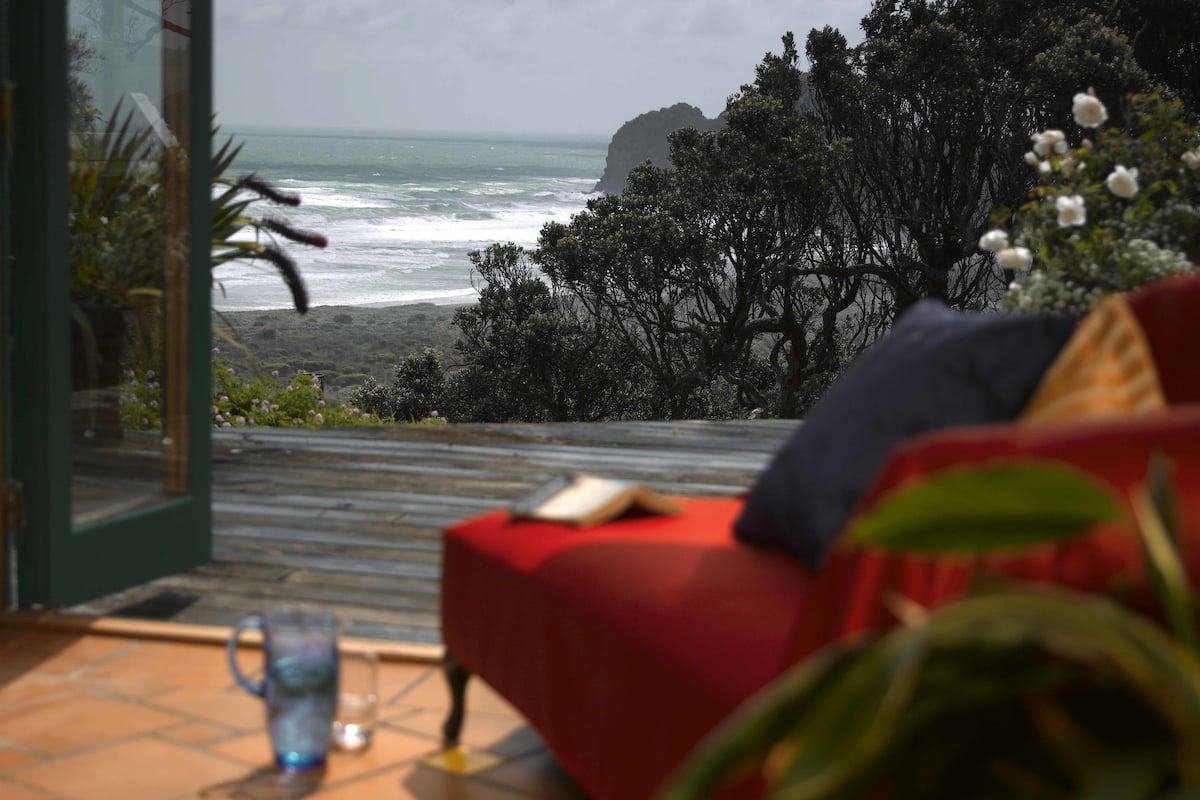 A room with a view of the ocean, a red sofa, and a glass table with a cup and saucer.