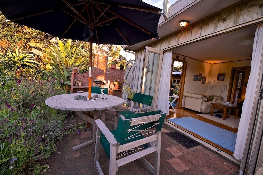 Un patio exterior con una mesa redonda y sillas, una sombrilla grande y vistas hacia la casa.