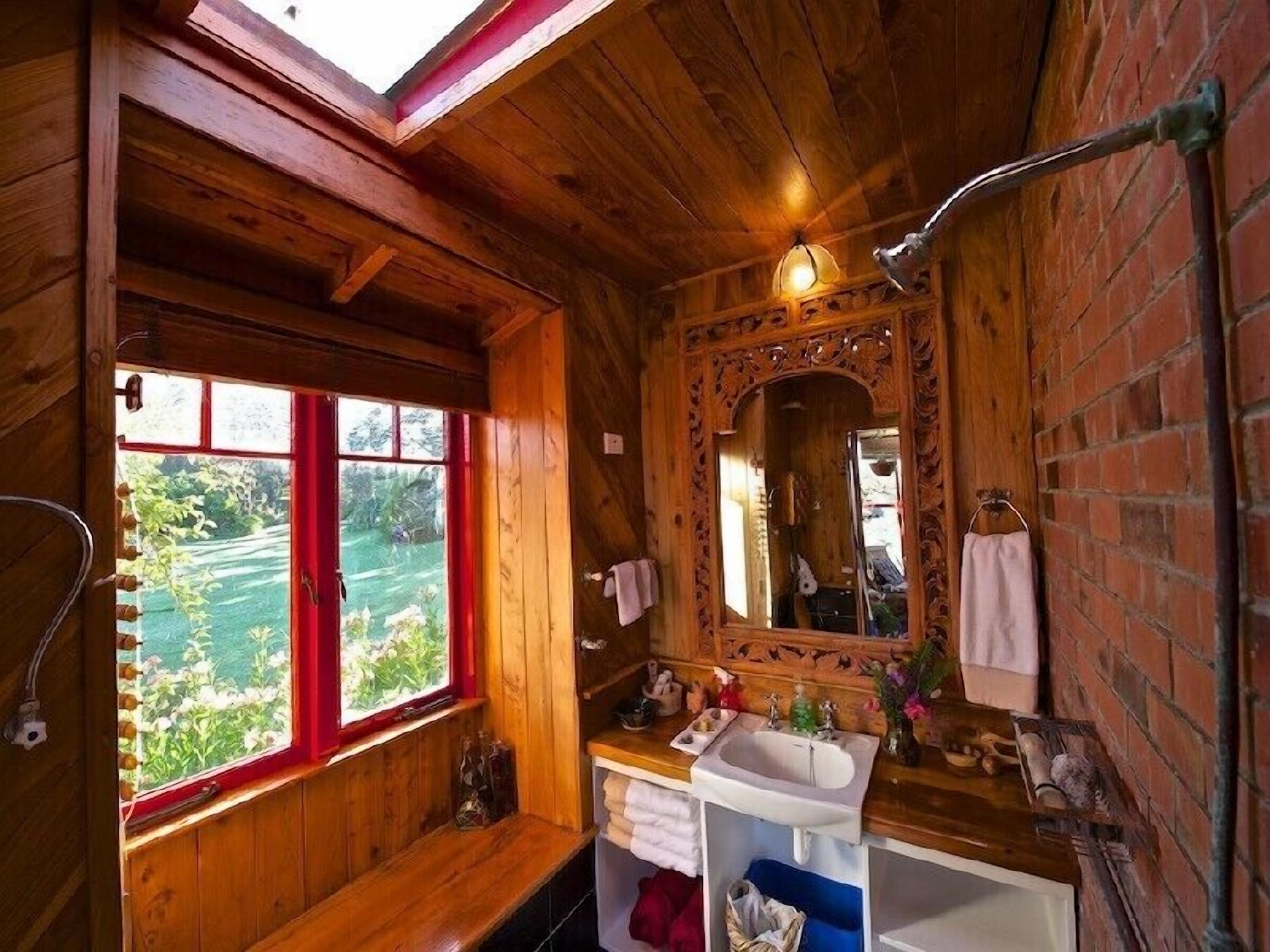 A wooden cabin bathroom with a skylight, a window, a sink, and a mirror.
