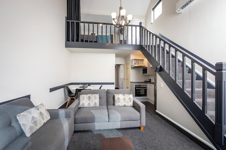 A modern living room with a grey sofa, a coffee table, and a staircase leading to an upper level.
