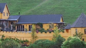 A castle-like building with a yellow exterior, a black roof, and a stone wall. - The Mudcastle (Upper Moutere)