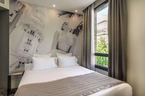 A hotel room with a large bed, a view of a building through the window, and a mural on the wall. - Hotel Sixteen Paris Montrouge (Montrouge)