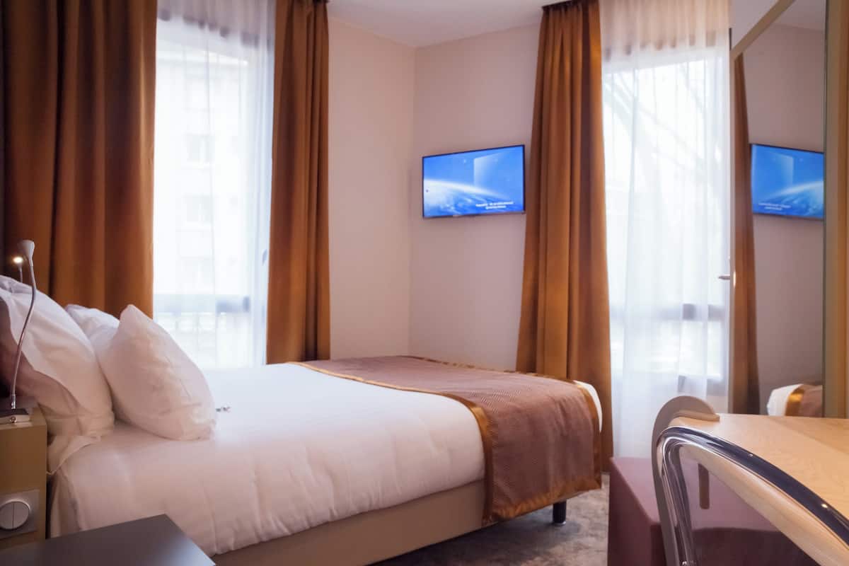 A hotel room with a bed, a desk, and two televisions mounted on the wall.