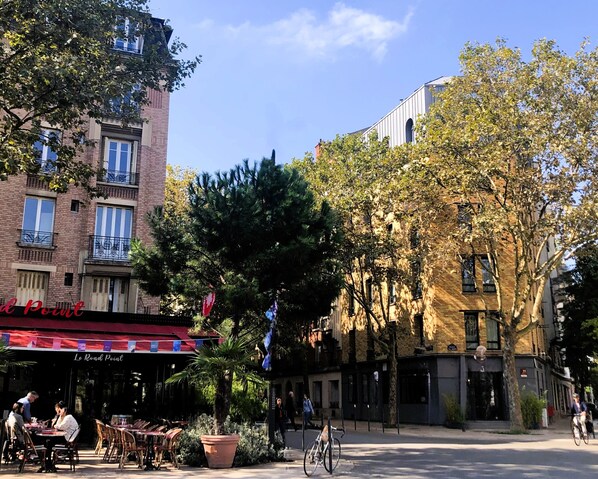 A café with outdoor seating, a bicycle parked nearby, and a tree in the foreground. - Hotel Sixteen Paris Montrouge (Montrouge)