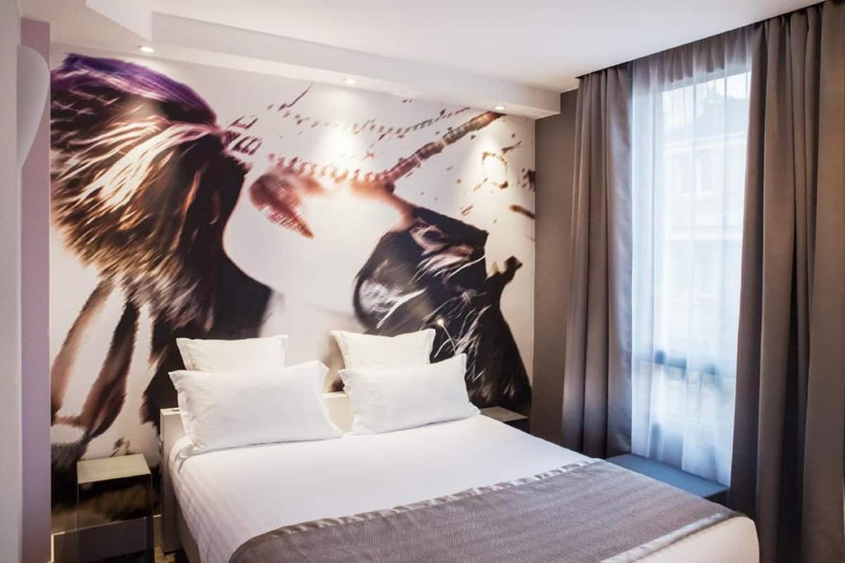 A modern hotel room with a large bed, white bedding, and a wall mural of a person playing a guitar.