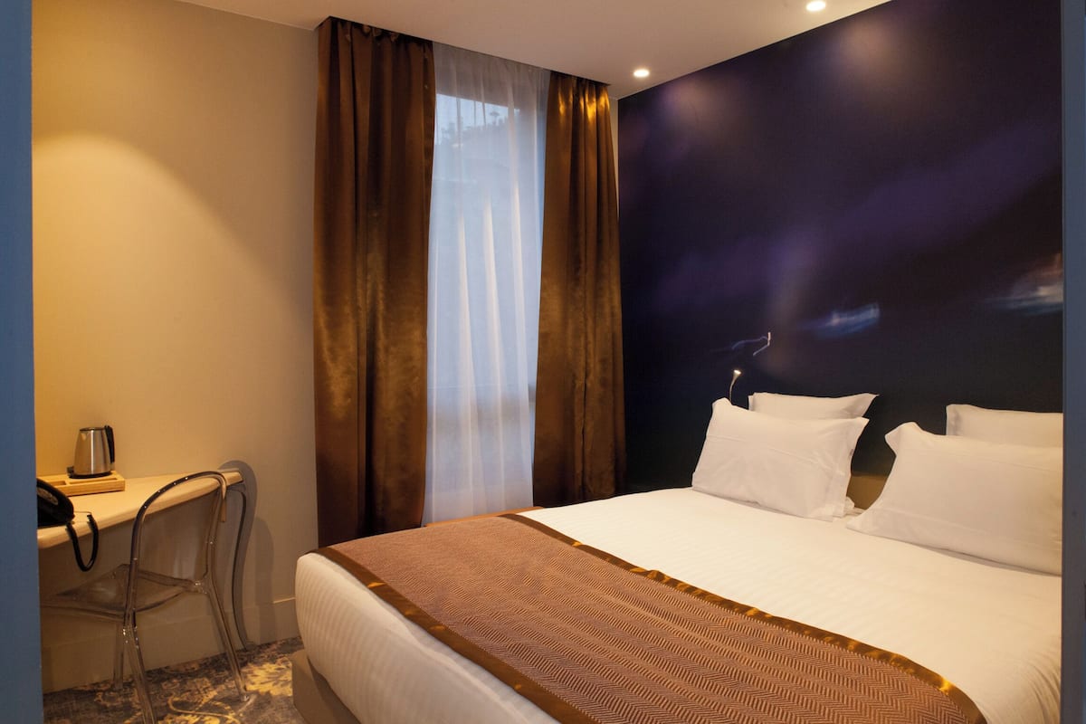 A hotel room with a bed, a desk, a chair, and a large window with curtains.