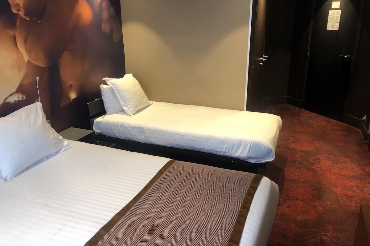 A hotel room with two single beds, a large poster on the wall, and a door with a sign.