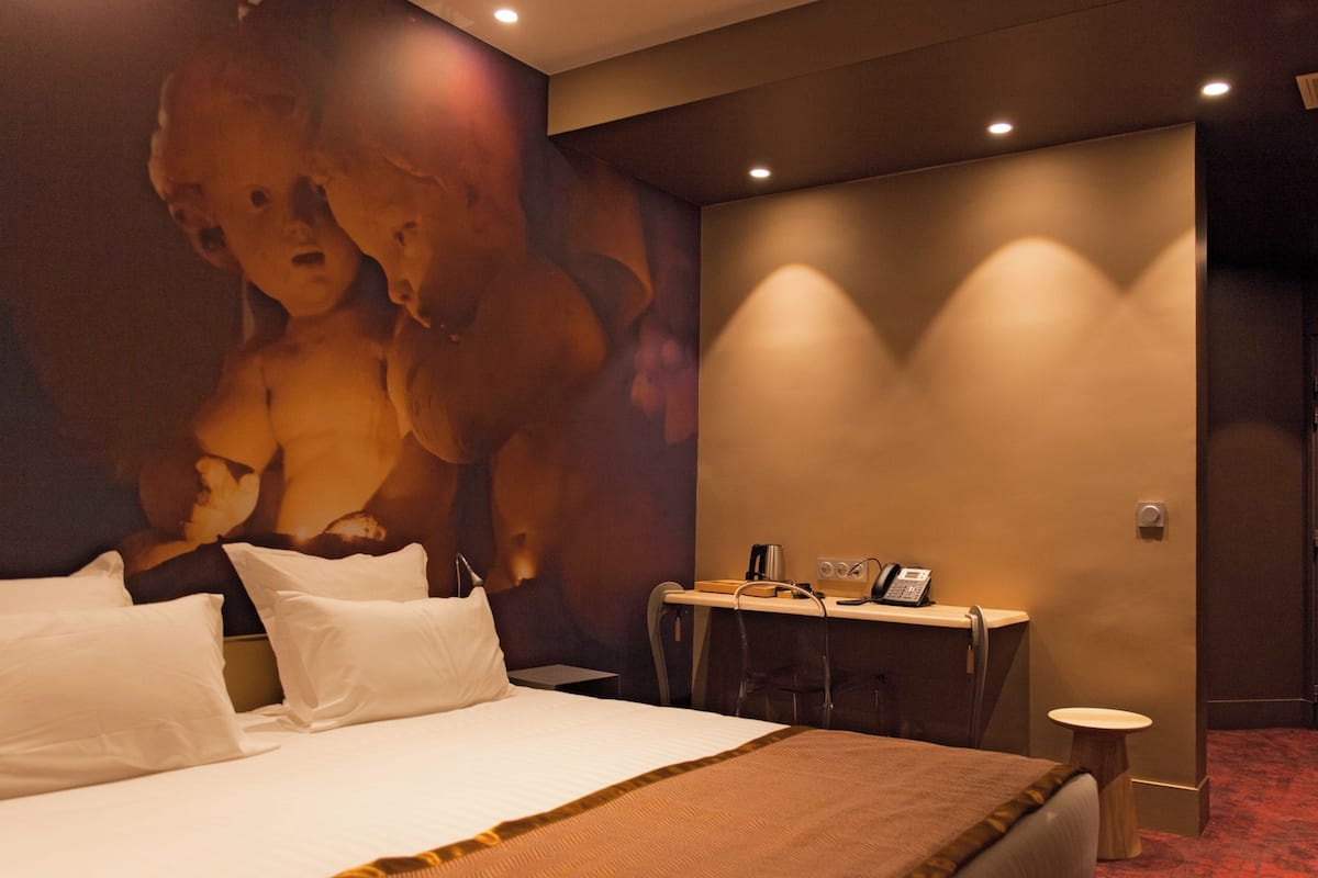 A hotel room with a large bed, a desk with a telephone, and a wall-mounted light fixture.