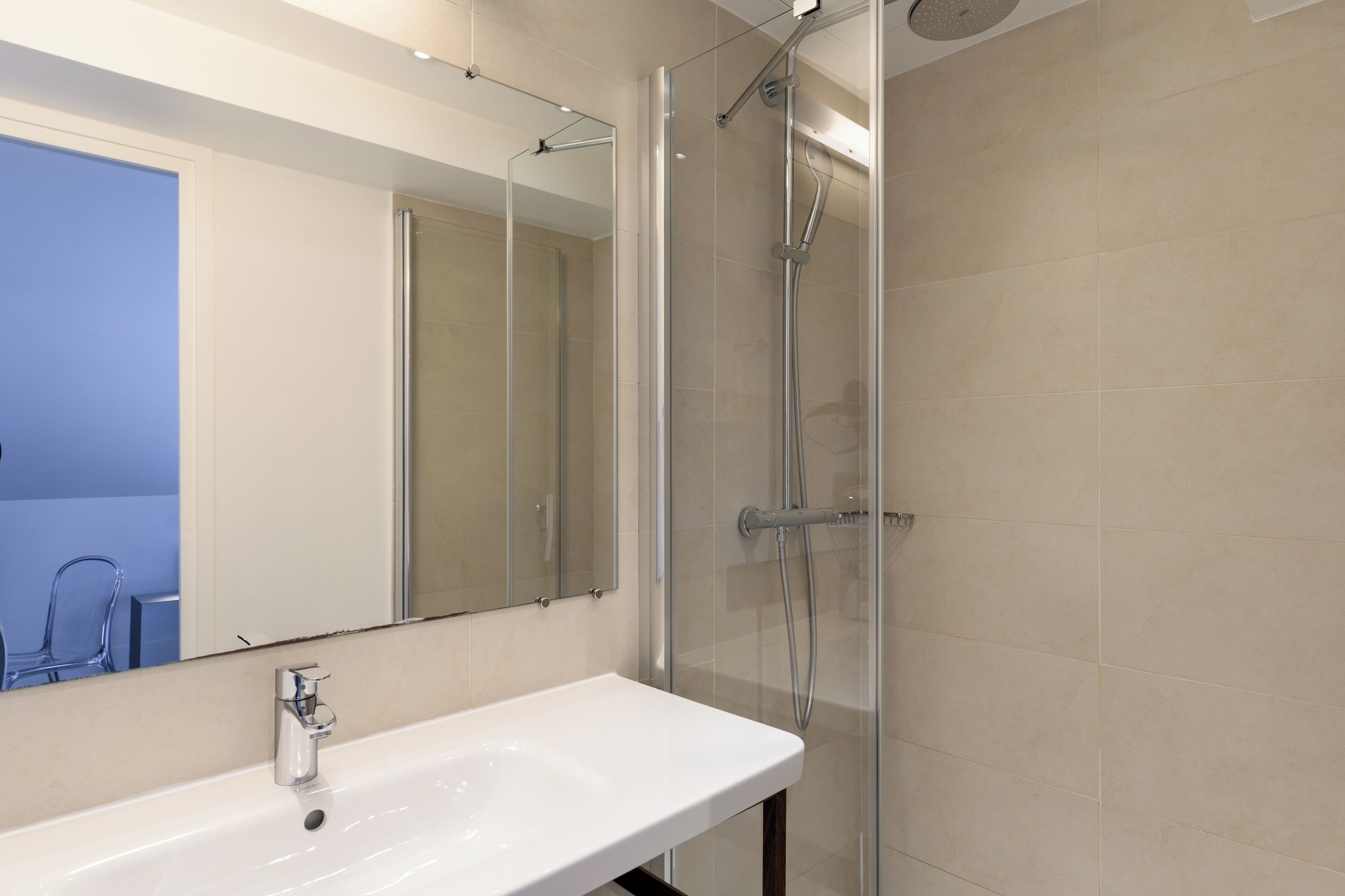 Bany amb un lavabo blanc, un mirall i una dutxa amb envàs de vidre.