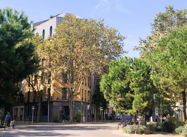 A street with a building featuring a large tree in front. - Hotel Sixteen Paris Montrouge (Montrouge)