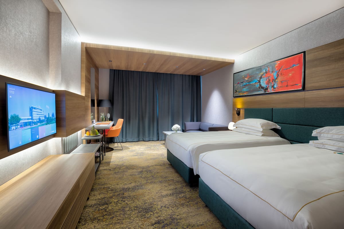 A hotel room with two beds, a desk, a television, and a painting on the wall.