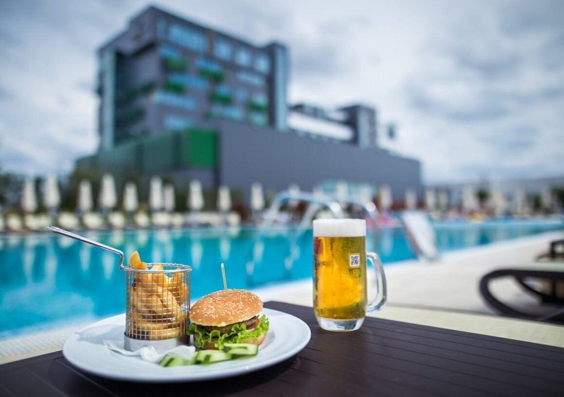 Una mesa de comedor con una hamburguesa, una jarra de cerveza y una cesta de papas fritas junto a una piscina.
