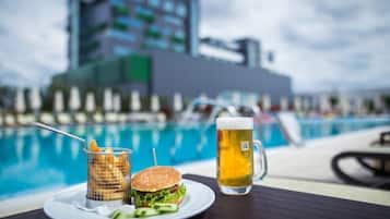 Una mesa de comedor con una hamburguesa, una jarra de cerveza y una cesta de papas fritas junto a una piscina.