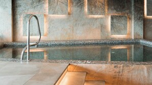 A modern spa area with a marble wall, a glass-bottomed pool, and a metal faucet. - Emerald Hotel Pristina, Kosovo (Preoce)