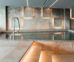 Un moderno espacio de spa con pared de mármol, piscina con fondo de cristal y grifo de metal.