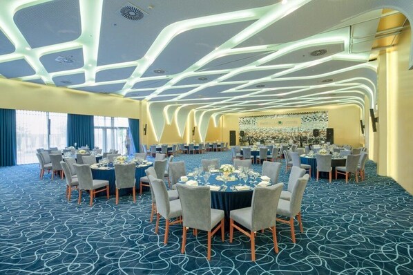 A large conference room with round tables, chairs, and a stage.