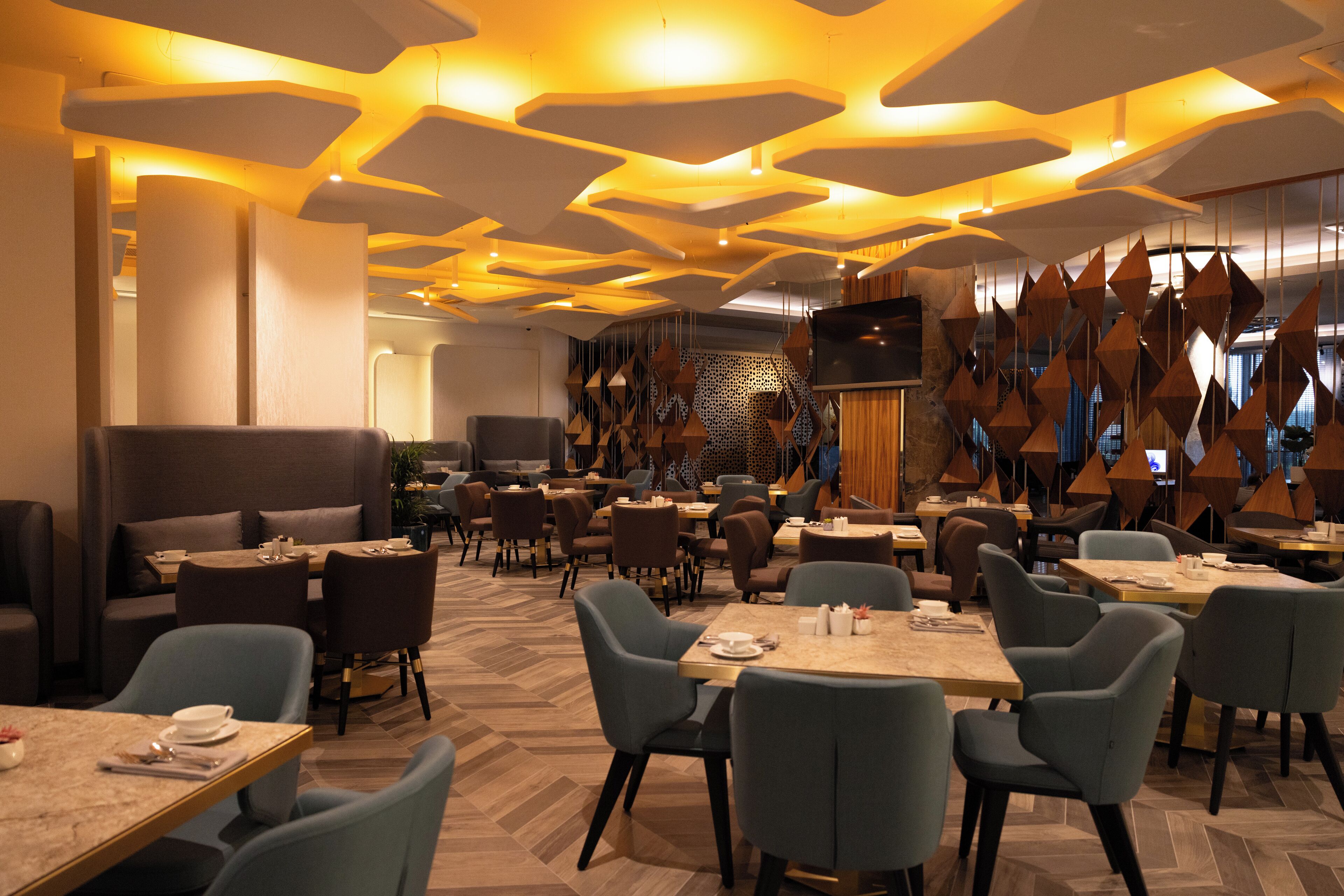 A modern restaurant with a geometric ceiling design, multiple dining tables, and chairs.