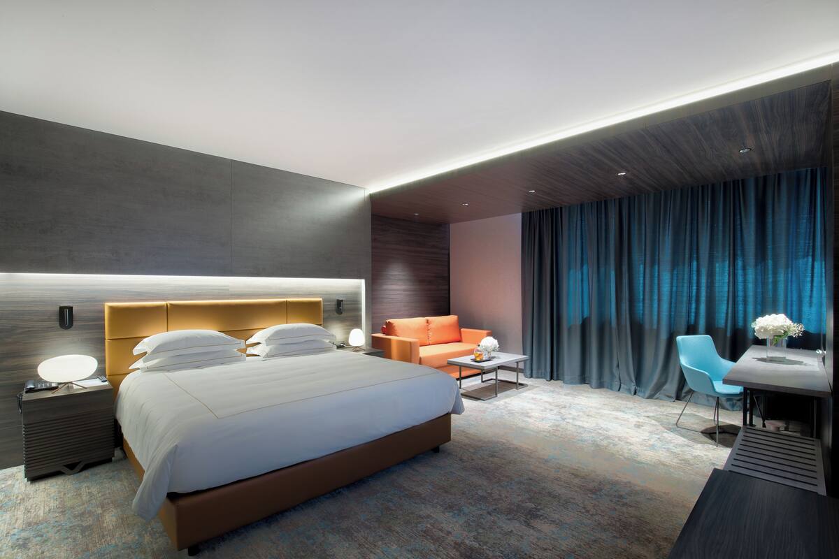 A modern hotel room with a large bed, a sofa, a desk, and a chair.