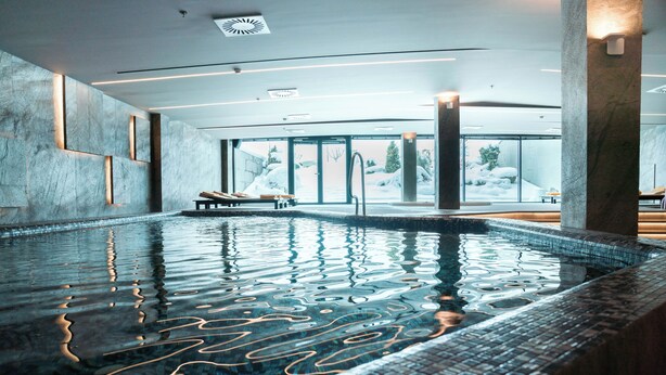 An indoor swimming pool with clear water, a tiled edge, and a bench. - Emerald Hotel Pristina, Kosovo (Preoce)