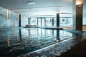 An indoor swimming pool with clear water, a tiled edge, and a bench.