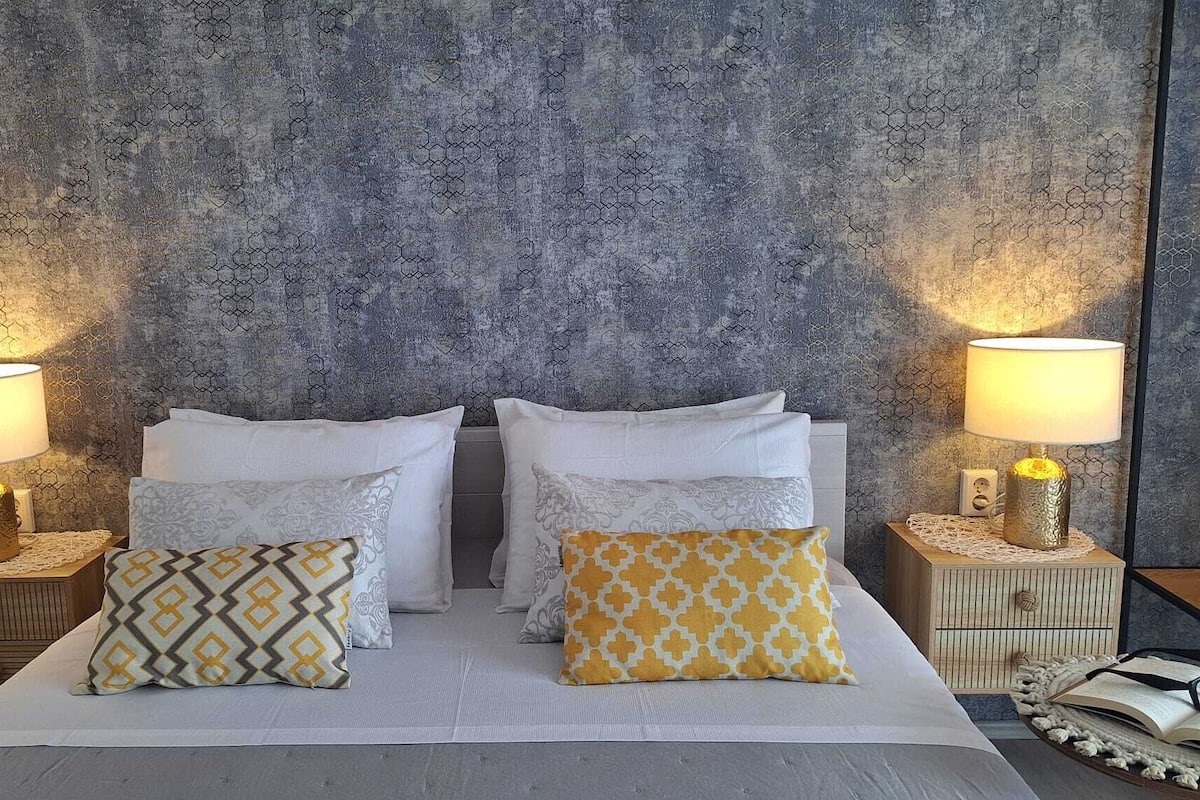 Ein Bett mit weißer Bettwäsche, zwei Nachttische mit Lampen sowie eine strukturierte Wand im Hintergrund.
