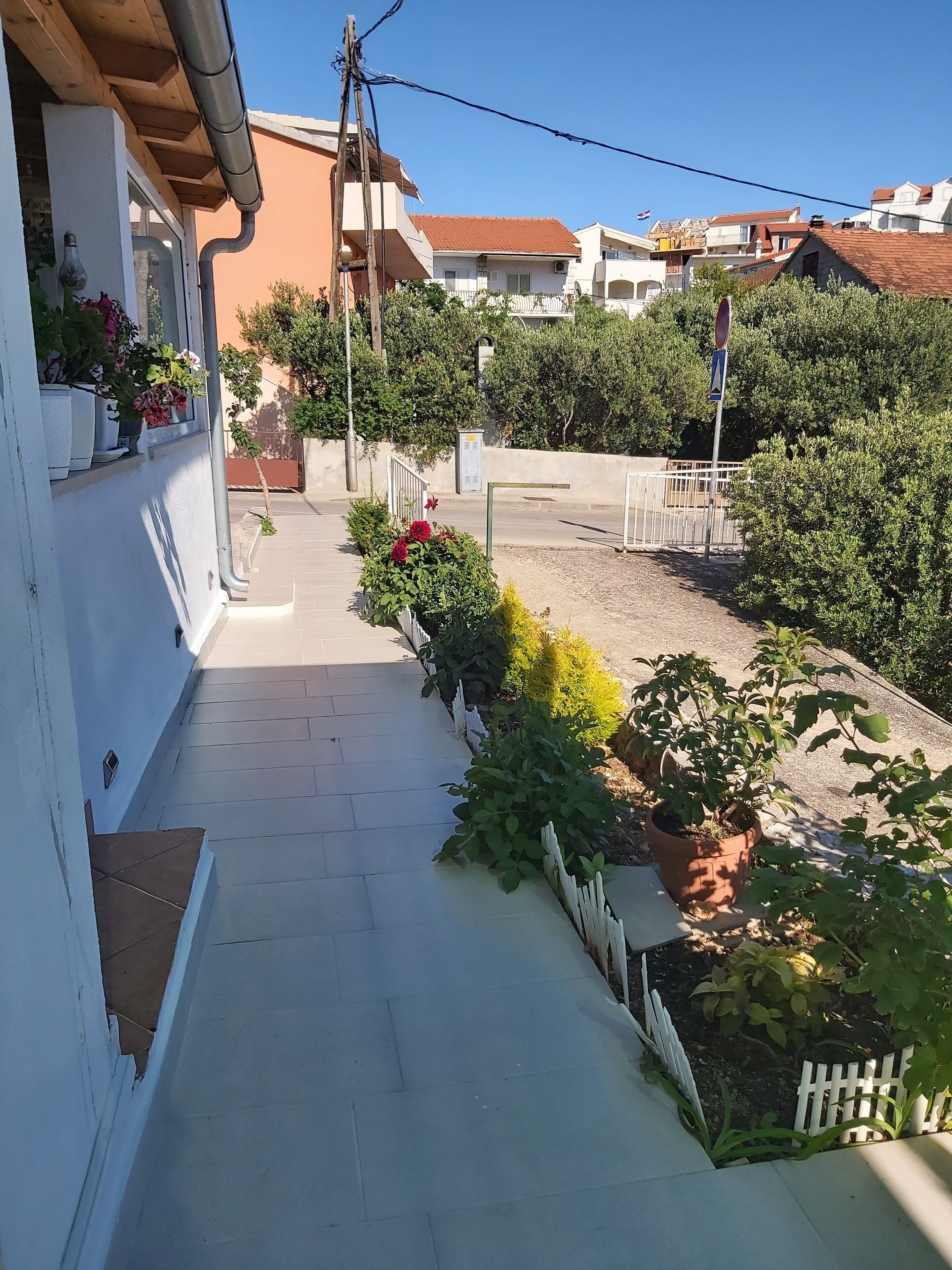 Un sentiero stretto che conduce a un edificio con facciata bianca e piante in vaso.