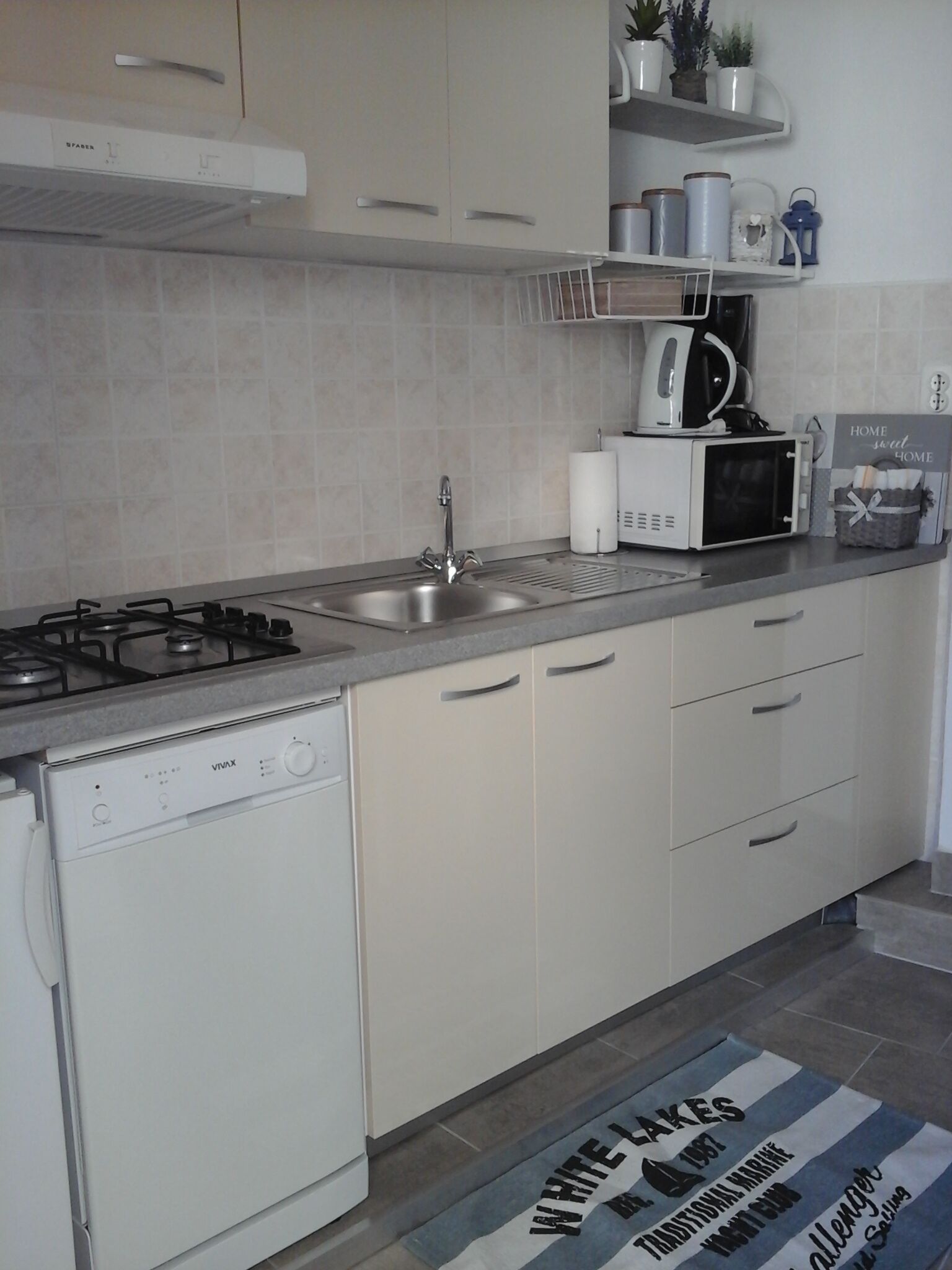 A modern kitchen with a gas stove, stainless steel sink, white cabinets, and a microwave.
