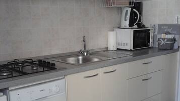 Una cocina moderna con estufa a gas, pileta de acero inoxidable, alacenas blancas y microondas.