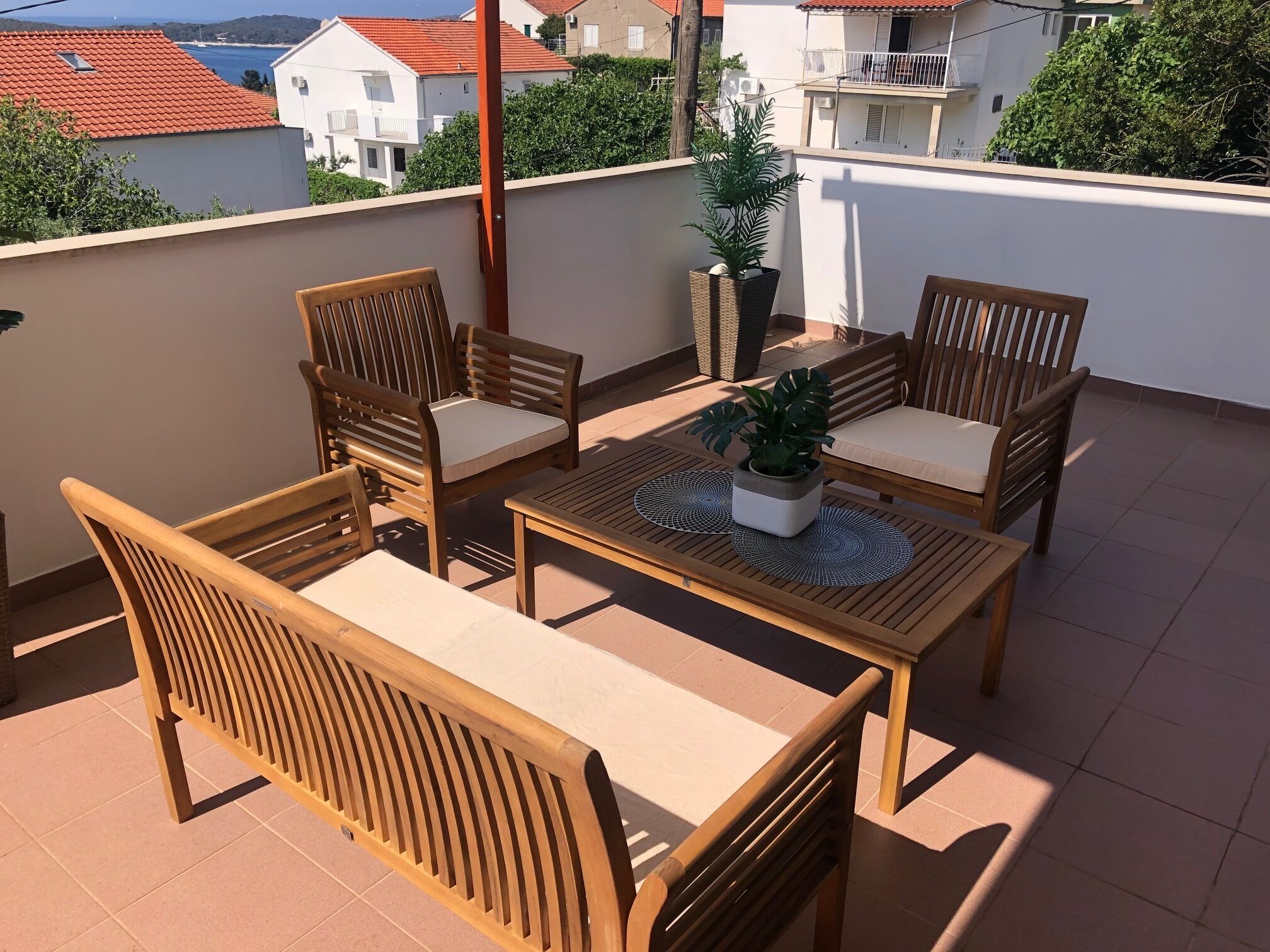 A wooden outdoor seating area with a table and chairs, a potted plant, and a view of buildings in the background.