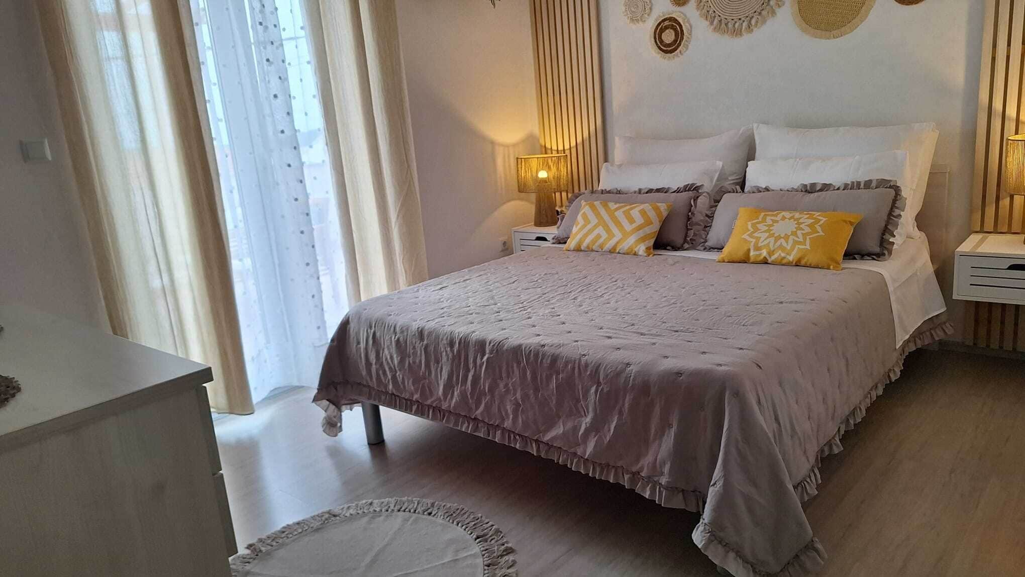 Un dormitorio con cama, mesitas de noche, lámpara y ventana con cortinas.