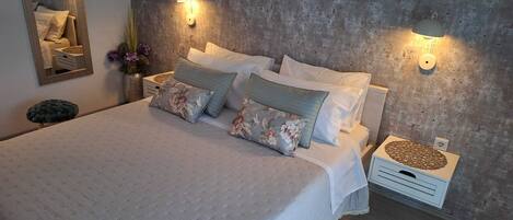 A neatly arranged bedroom with a large bed, two wall-mounted lamps, and a small bedside table with a decorative item.