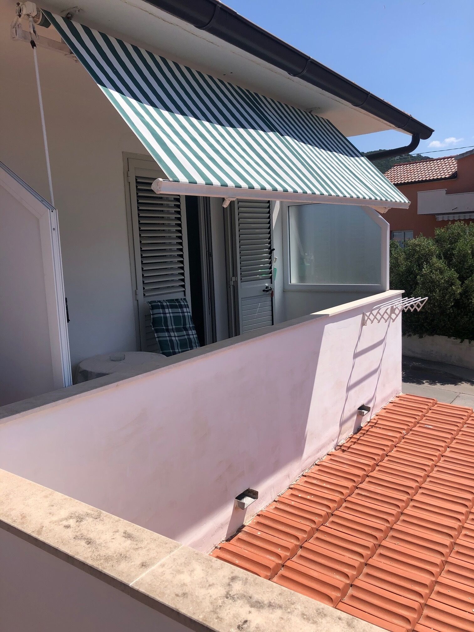 Un edificio residencial con un toldo a rayas, puerta de cristal corrediza y techo de tejas.
