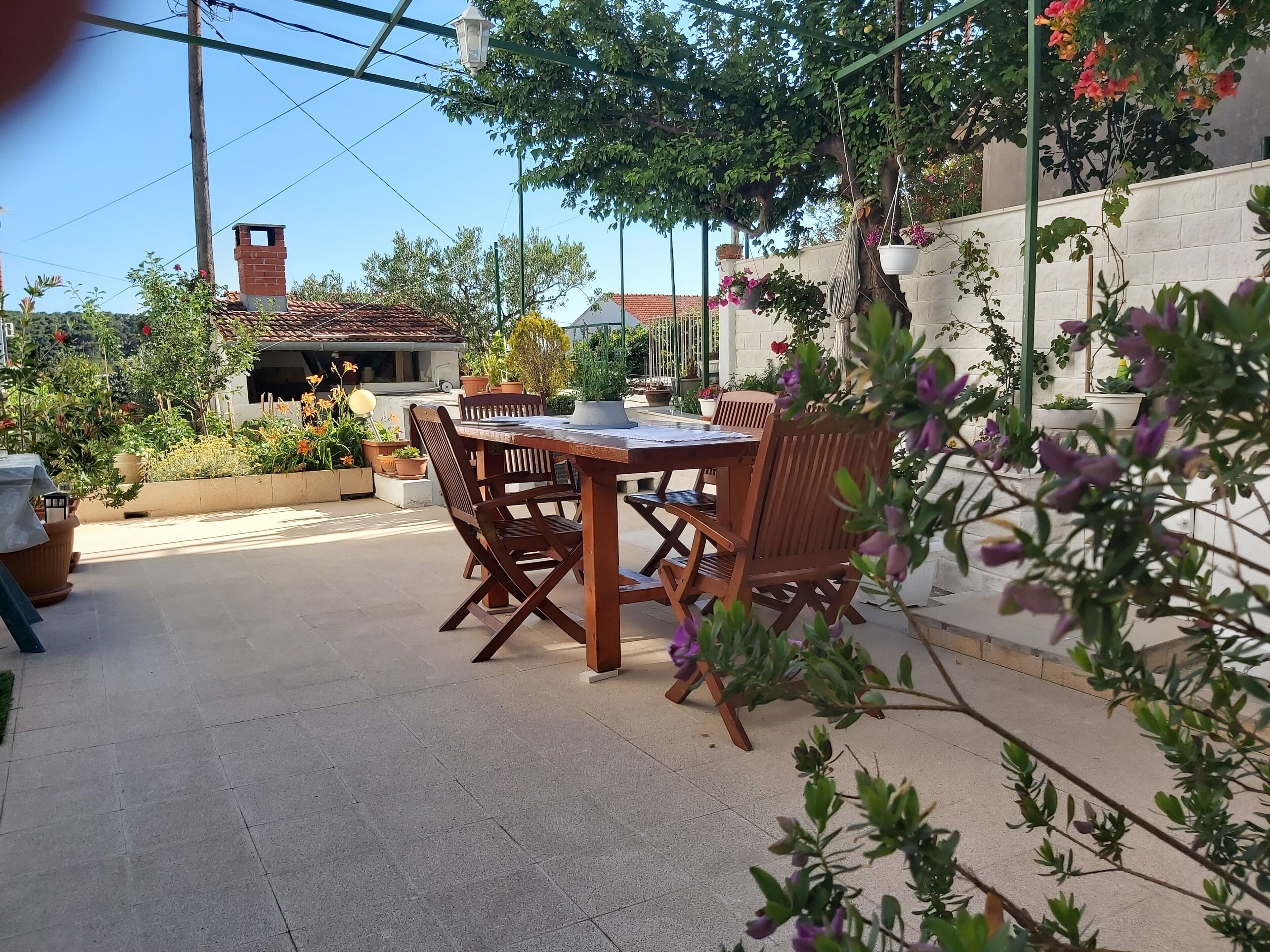An outdoor patio with a wooden table and chairs, surrounded by potted plants and a brick wall.