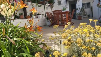 A patio area with a wooden table and chairs, surrounded by potted plants and flowers.