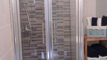 A glass-enclosed shower with a tiled wall, a handheld showerhead, and a control panel above the shower.