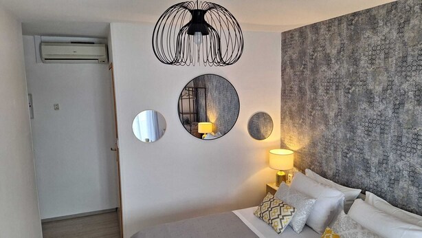 A bedroom with a bed, a wall-mounted lamp, and three circular mirrors. - Apartmani Teo (Hvar)
