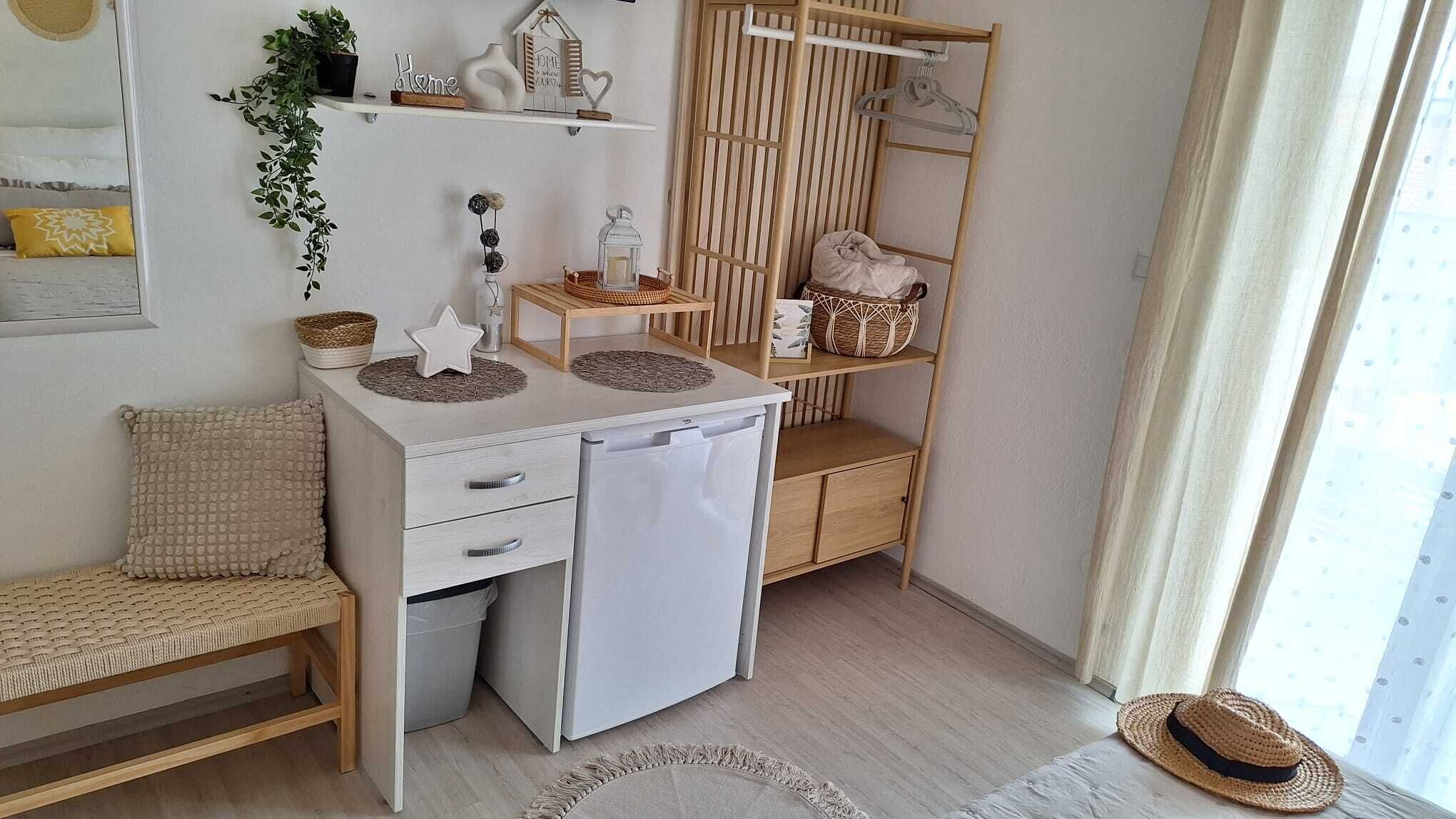 Ein kompakter, gut eingerichteter Raum mit einem Bett, einem kleinen Schreibtisch mit Kühlschrank, Regalen mit Dekoration und einem Fenster mit Vorhängen.
