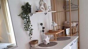 A modern, well-lit room with a wooden desk, a bench with a woven seat, a television mounted on the wall, and a shelf with decorative items. - Apartmani Teo (Hvar)