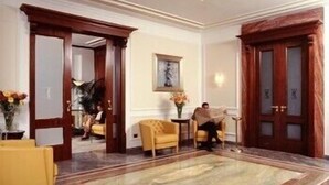 A spacious lobby with a large marble floor, a yellow armchair, and a wooden door. - Hotel Civita (Atripalda)