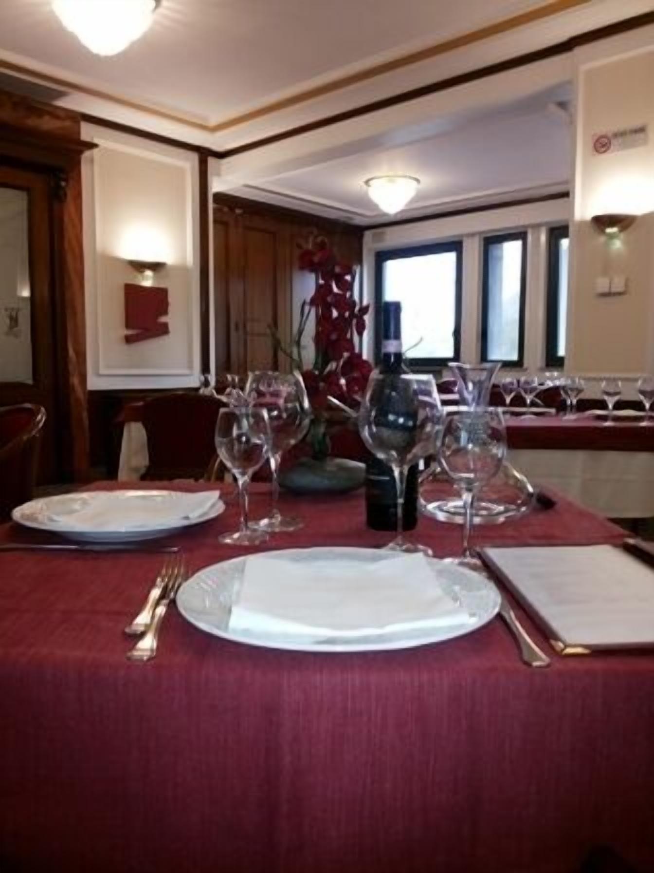 A dining table set with plates, cutlery, and wine glasses, with a vase of flowers and a bottle of wine in the center.